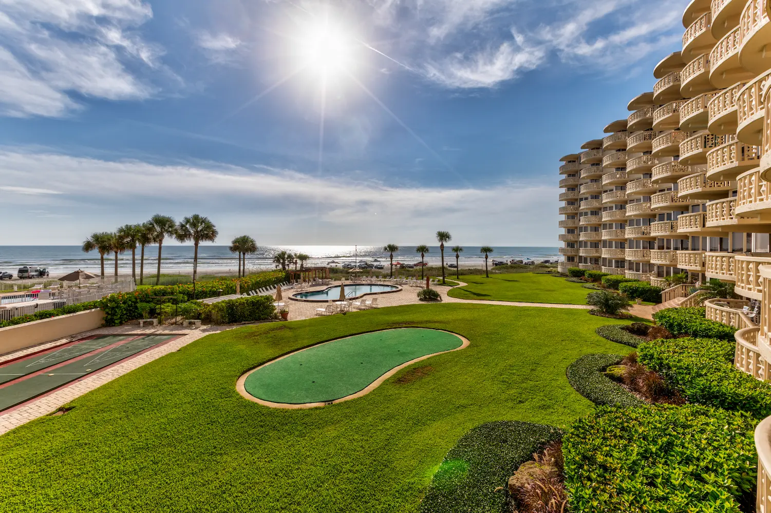 Oceanfront condo community exterior in New Smyrna Beach, Florida, providing context for a coastal condo renovation project by Newberry Homes. Large grassy area next too pool , games, and the ocean.