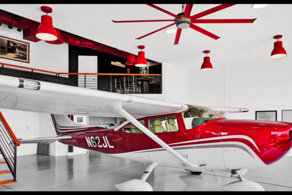 Hangar home with red passenger plane parked in garage with matching red overhead lights and ceiling fan