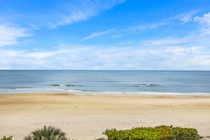 Wide view of the Atlantic Ocean and uncrowded sandy beach under a blue sky, seen from an oceanfront condo remodeled by Newberry Homes in Ponce Inlet, Florida.
