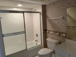 Before bathroom remodel featuring original tub shower and outdated finishes including sea shell wall tiles, before transformation by Newberry Homes south of Daytona Beach in New Smyrna Beach