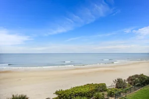 Sweeping view of the Ponce Inlet coastline with gentle surf and a wide sandy beach beside an oceanfront condo remodeled by Newberry Homes in Florida.