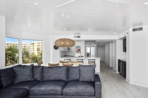 Open floor plan living and dining space with a navy sectional, a woven pendant light, and shiplap ceiling detailing in a coastal condo remodel by Newberry Homes in Ponce Inlet, Florida.