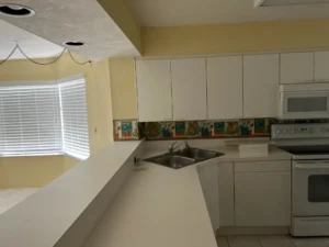 Before photo of dated condo kitchen with laminate countertops and older cabinetry prior to renovation in New Smyrna Beach, Florida.