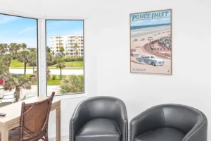 Cozy sitting area with leather club chairs and a vintage Ponce Inlet, Florida poster beside a window overlooking the coastal community, in a condo remodel by Newberry Homes.