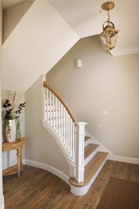 Curved staircase with white balusters, wood handrail, and lantern pendant lighting in a custom design build home in Ponce Inlet, Florida by Newberry Homes
