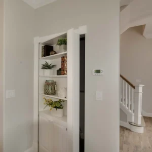 Custom hidden bookcase integrated into a wall with built-in shelving and trim details in a custom design and build home by Newberry Homes. The staircase is peeking out behind the hidden bookcase.