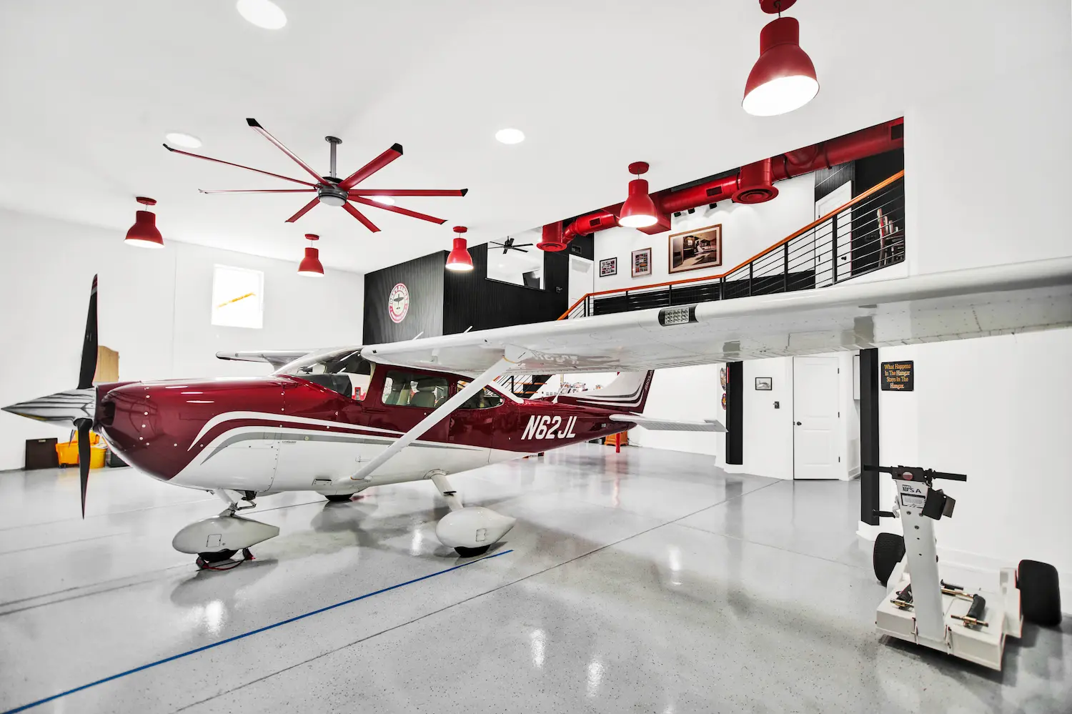 Custom hangar home by Newberry Homes in the Spruce Creek aviation community in Central Florida featuring a single-engine airplane inside a spacious residential aircraft hangar with polished concrete floors, mezzanine living space, modern industrial lighting, and high ceilings.