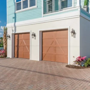 Two-car garage with wood-look garage doors, brick paver driveway, and coastal exterior finishes in a design build home in Ponce Inlet, Florida by Newberry Homes