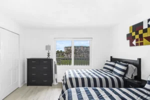 Guest bedroom with two beds in navy and white striped bedding, a black dresser, and nautical flag wall art in a condo remodel by Newberry Homes in Ponce Inlet, Florida.