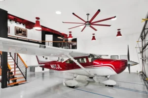 Cessna airplane parked inside a custom Newberry Homes hangar home garage in Port Orange, Florida, with a two-story black steel mezzanine bar loft, red industrial ductwork, and matching red pendant lighting