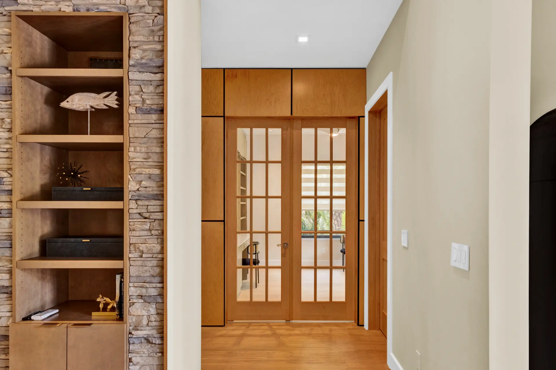 Japandi-inspired custom home entryway beautiful french style doors with warm wood tones, built-in shelving, and stone accents by Newberry Homes in New Smyrna Beach, Florida.