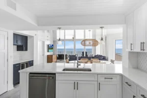 Remodeled kitchen island with white quartz countertops, stainless steel appliances, and pendant lighting overlooking the ocean-view living area in a Ponce Inlet condo by Newberry Homes