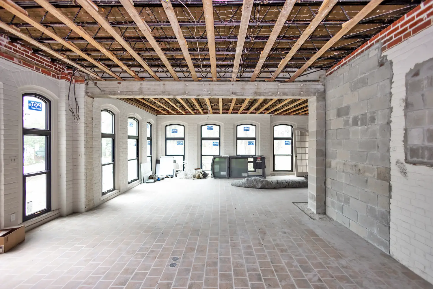 Interior remodel construction phase in Central Florida showing exposed ceiling framing, brick walls, structural beam installation, and unfinished flooring during renovation of luxury custom home build.