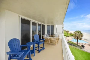 Private oceanfront balcony with blue Adirondack chairs and rattan seating overlooking the community pool and beach in a condo remodel by Newberry Homes in Ponce Inlet, Florida.