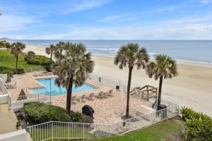 Oceanfront community pool and sundeck framed by palm trees overlooking the beach at the Oceanquest condominium in Ponce Inlet, Florida.