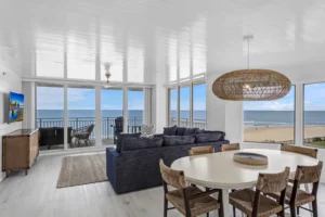 Oceanfront great room combining living and dining areas with wraparound ocean views, a navy sofa, and an oversized woven pendant light in a condo remodel by Newberry Homes in Ponce Inlet, Florida.