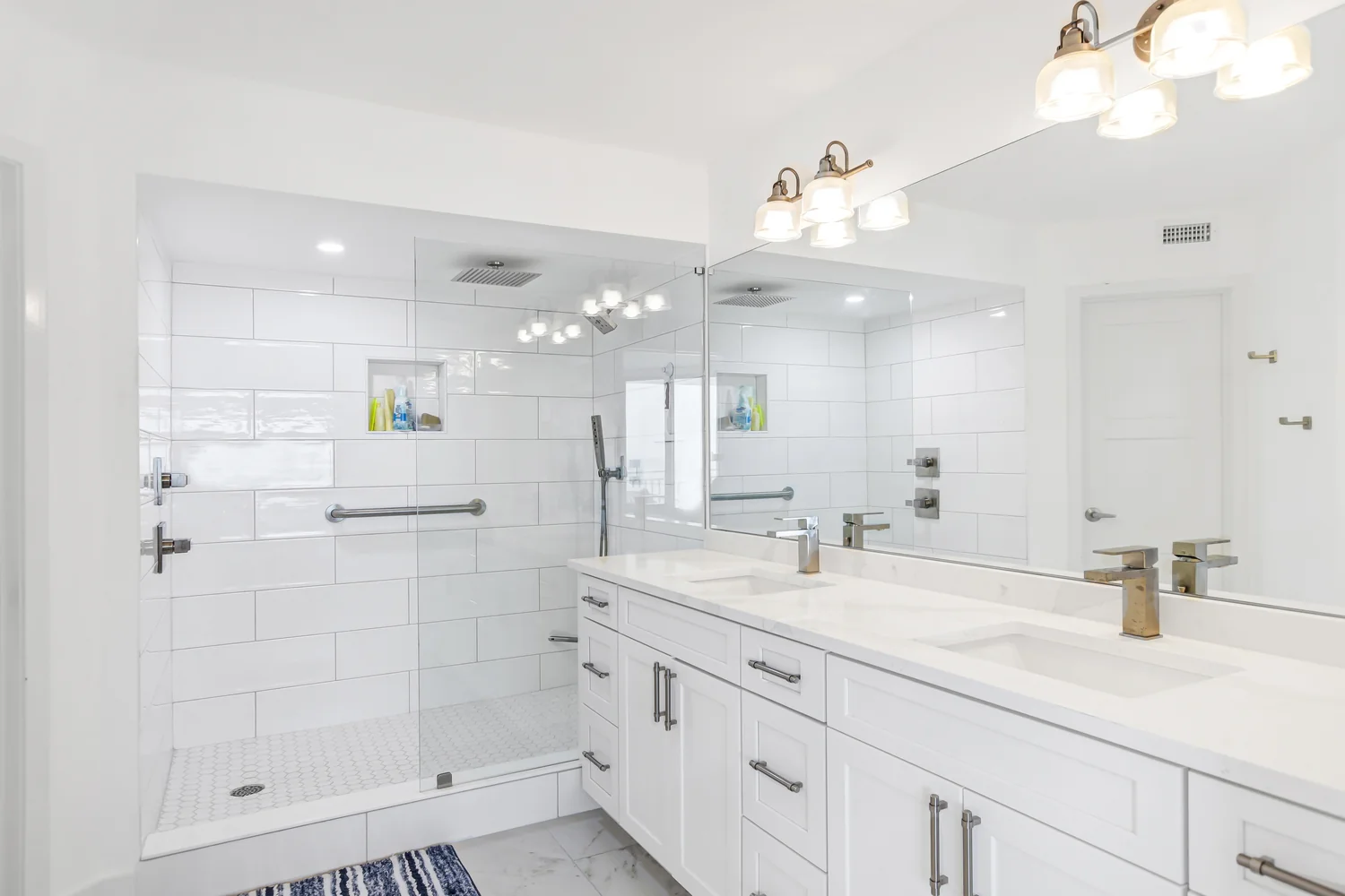 Primary bathroom remodel featuring an expansive glass walk-in shower, white subway tile, and a double vanity with quartz countertops in a Ponce Inlet condo by Newberry Homes.