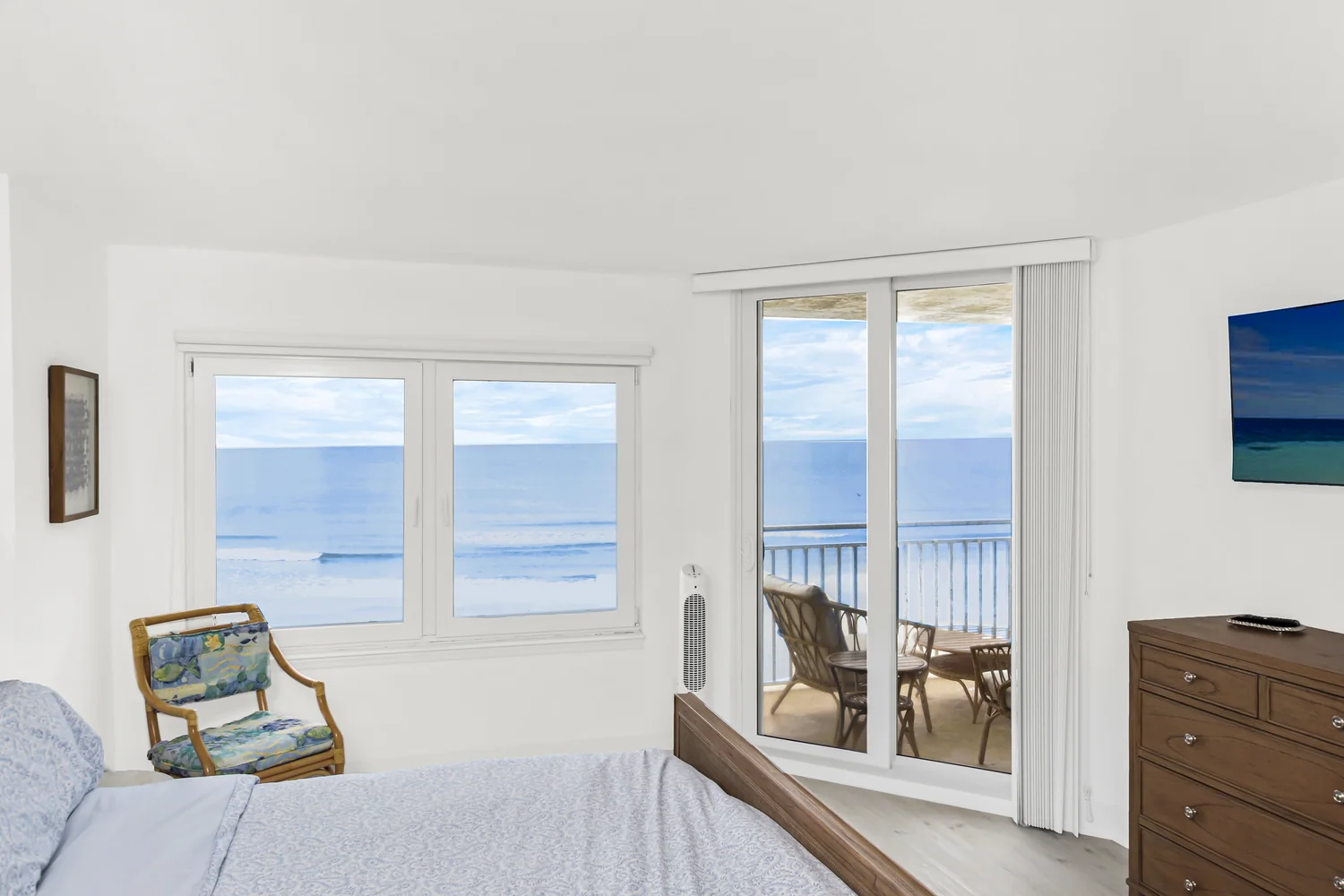 Primary bedroom with floor-to-ceiling ocean views, sliding glass doors to a private balcony, and a wall-mounted TV in an oceanfront condo remodel by Newberry Homes in Ponce Inlet, Florida.