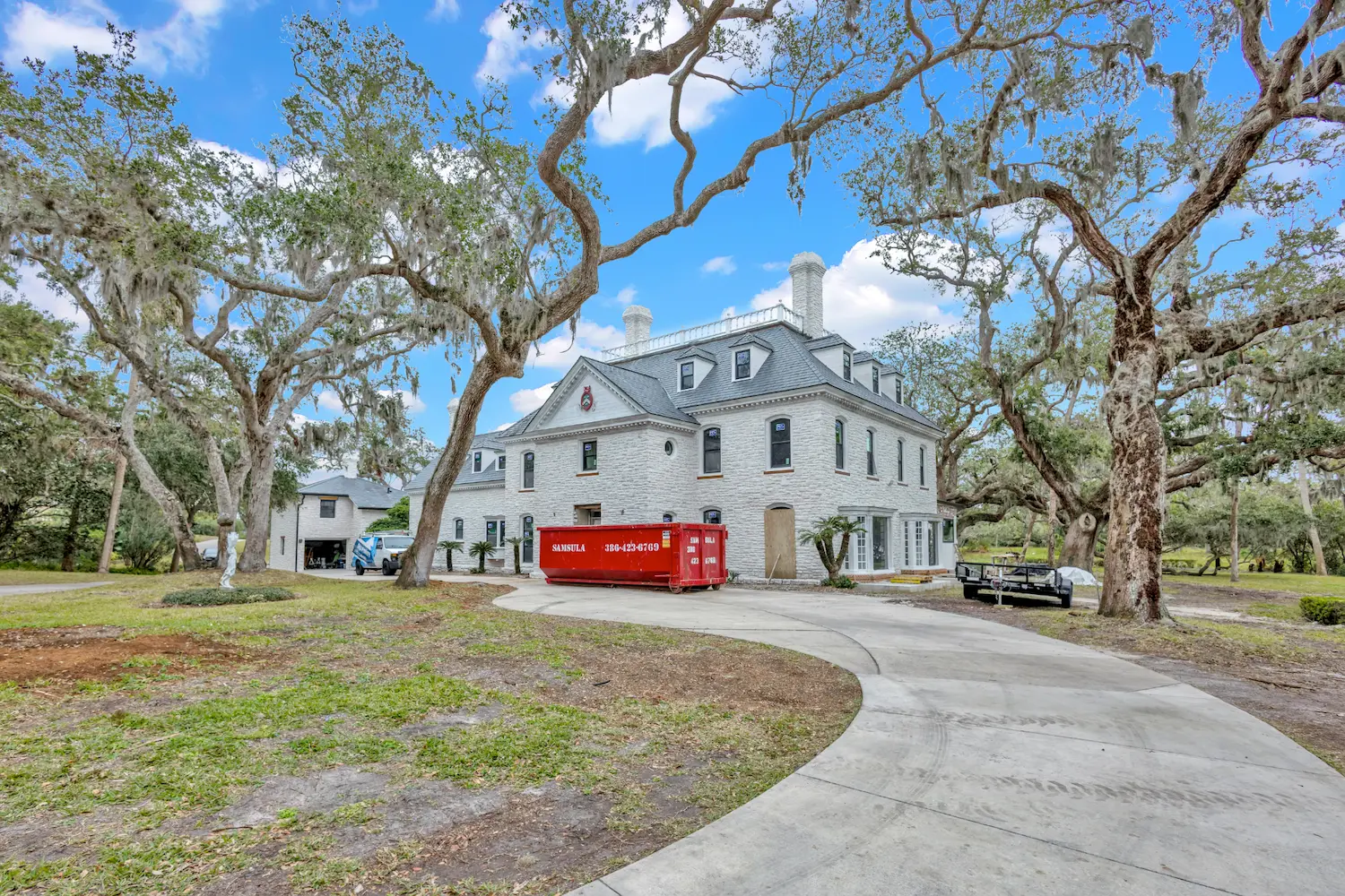 Coastal home remodeling project by Newberry Homes in Daytona Beaech Florida - exterior round driveway surrounded by trees leading up to the home, construction equipment, facing brick home with over 12 windows,
