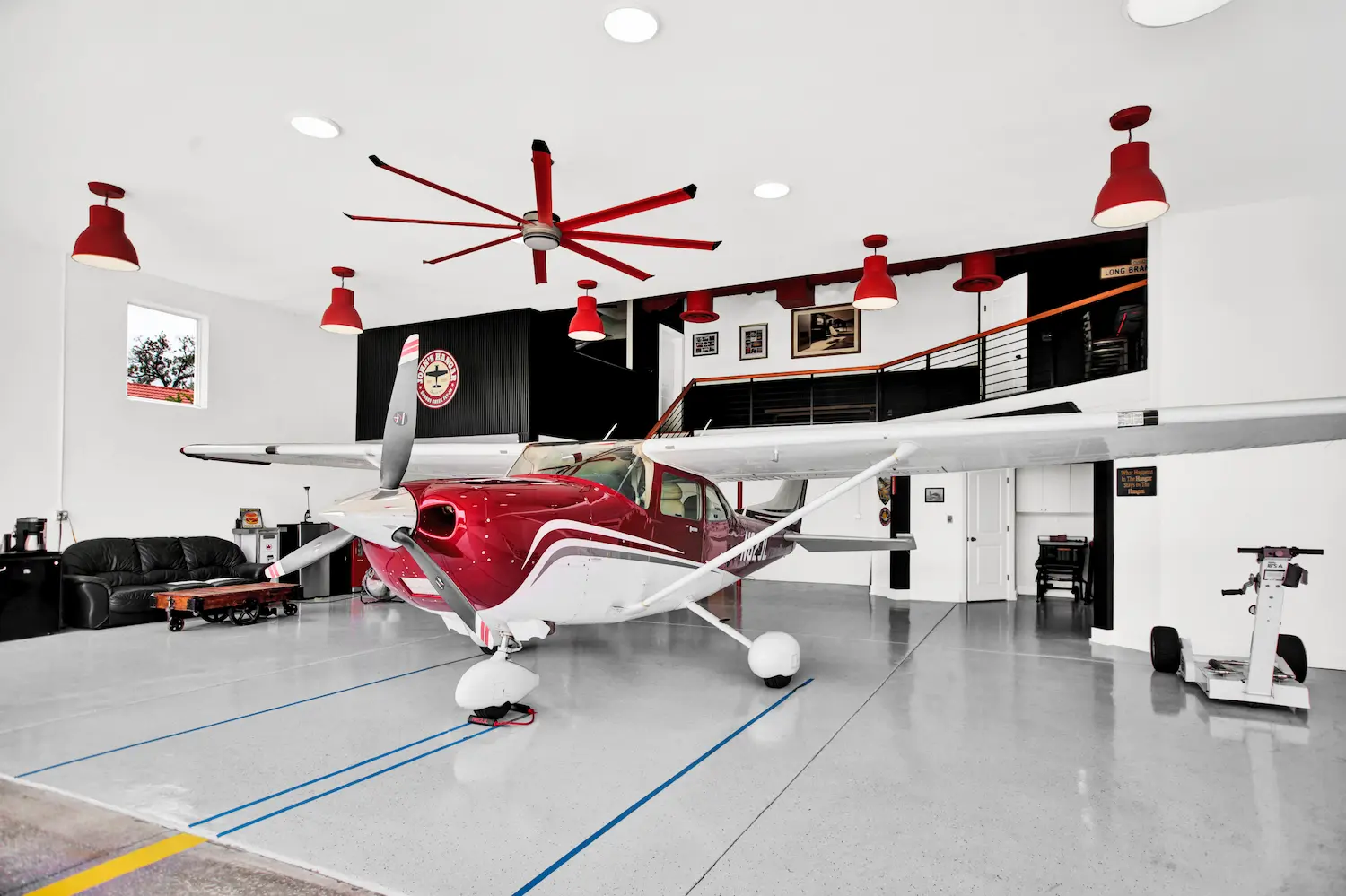 Spacious custom hangar home by Newberry Homes in the Spruce Creek aviation community in Central Florida featuring a single-engine airplane parked inside a luxury residential aircraft hangar with polished concrete floors, loft overlooking the hangar, and modern industrial lighting.