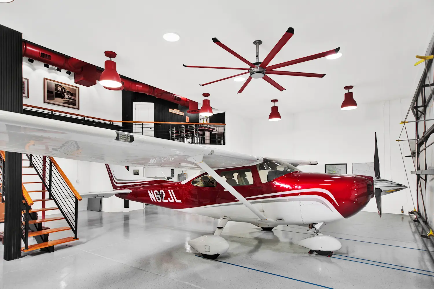 Luxury hangar home by Newberry Homes in the Spruce Creek aviation community in Central Florida featuring a red-and-white single-engine airplane parked inside a modern aircraft hangar with mezzanine, industrial lighting, and polished concrete floors.