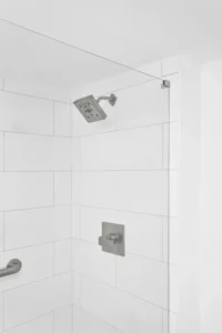 Detail of a walk-in shower with vertical white subway tile, a modern square rainfall showerhead, and brushed nickel fixtures in a Ponce Inlet condo remodel by Newberry Homes.