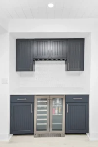 Custom wet bar with navy blue beadboard cabinetry, a white picket tile backsplash, and a dual-zone wine and beverage refrigerator in a condo remodel by Newberry Homes in Ponce Inlet, Florida