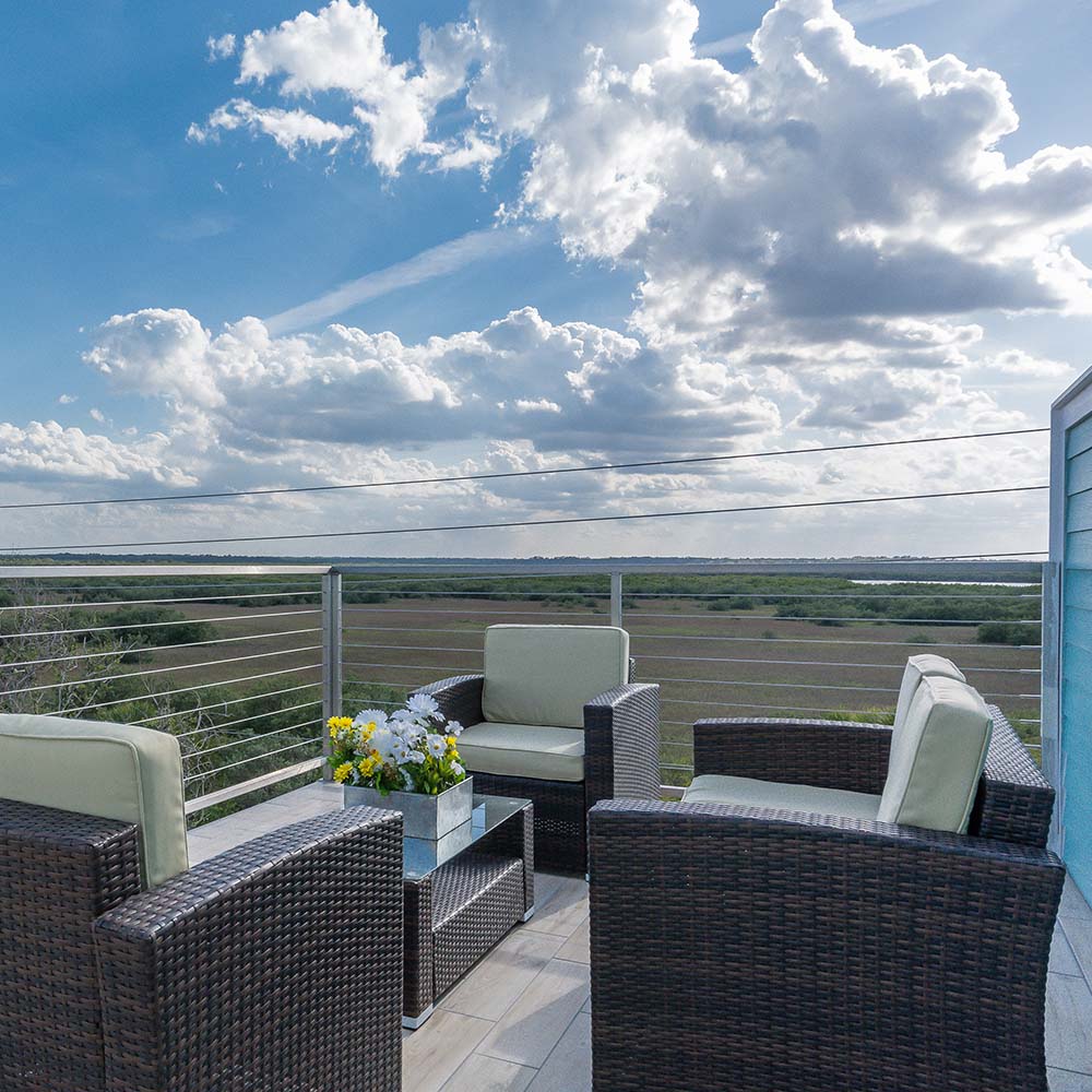 outdoor patio with three cushioned chairs and blue sky with white rolling clouds overhead