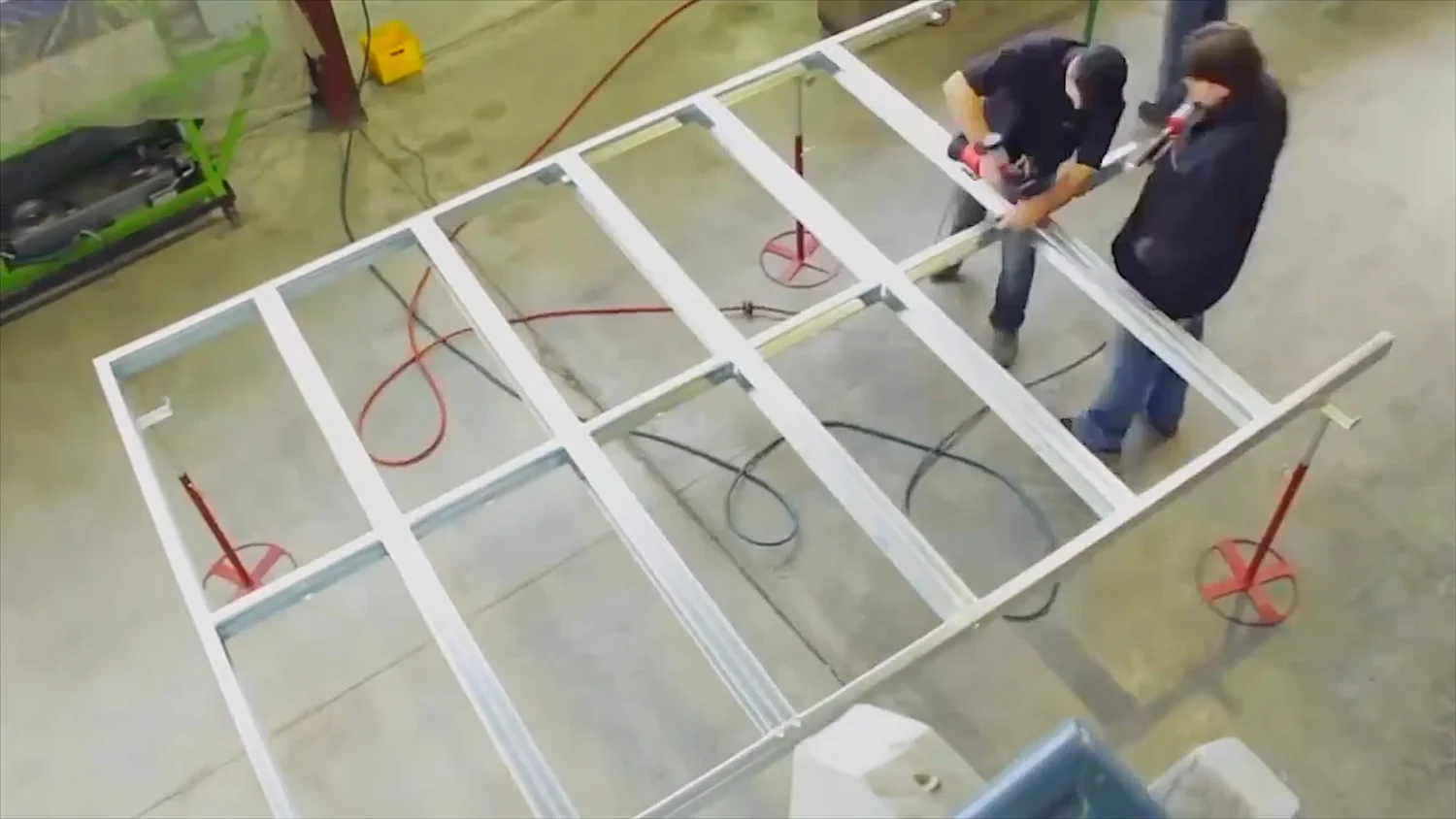 Two workers assembling a light gauge steel wall frame panel on a factory floor with pneumatic tools and red air hose
